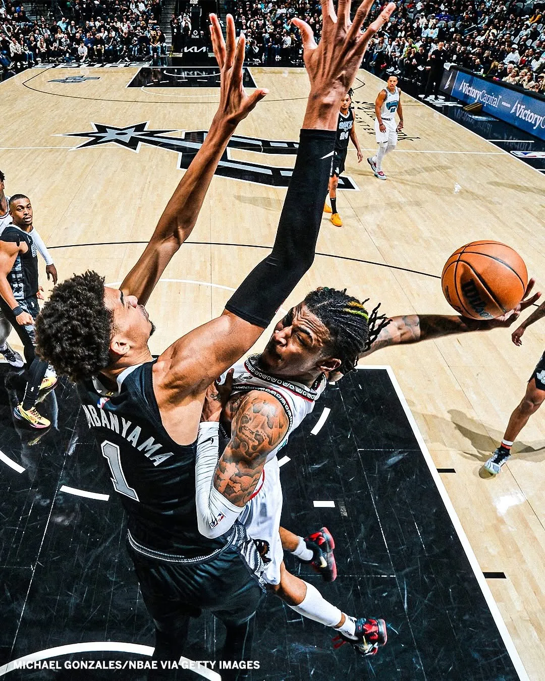 Deux joueurs de basket au duel sous le panier, l'un contestant le tir de l'autre au-dessus du cercle